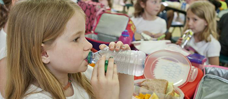 Water is a Healthy Drink: A young elementary school aged girl takes a drink from a chilled water bottle during lunch.