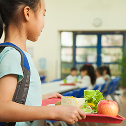 Elementary school girl holding a tray filled with a healthy lunch in the school cafeteria.