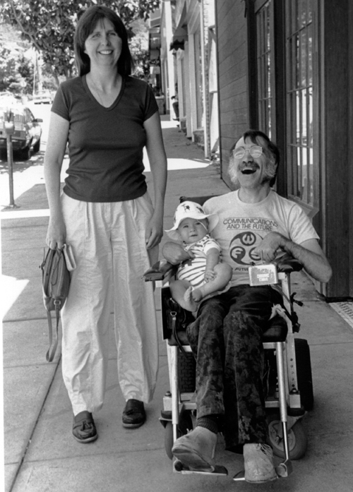 Photo of woman next to  man in wheelchair holding baby