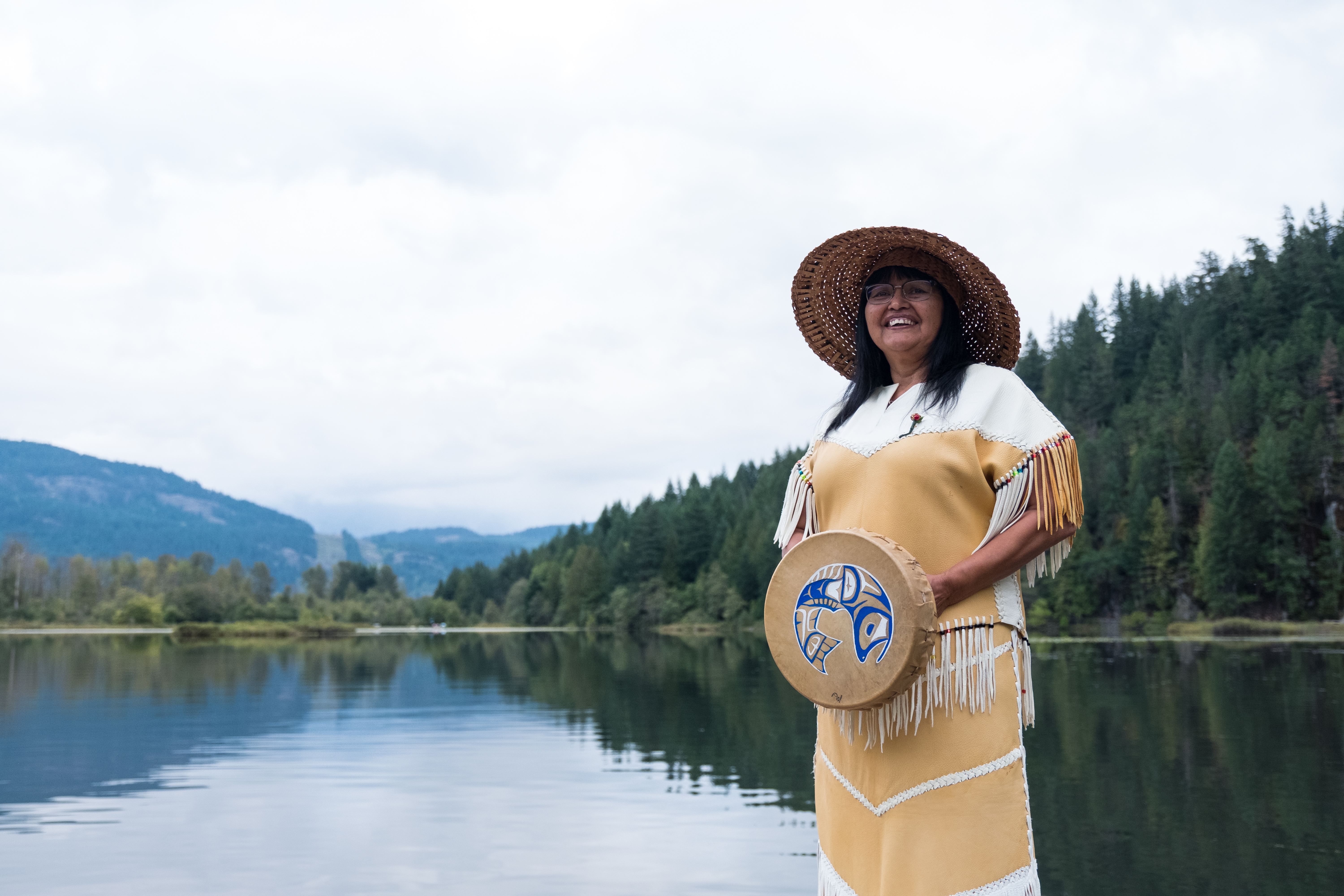 Woman holding an Alaska Native drum in front of a lake